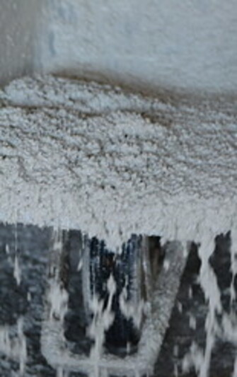 Nahaufnahme von frischem, sehr leichtem Beton (Leichtbeton) mit deutlich sichtbaren, groben, weißen Zuschlagstoffen. Die Masse wirkt porös und locker, Wasser läuft an den Rändern ab und tropft von der Kante. Die Struktur ist offen und erinnert an grobkörnigen Schaum oder Bimsbeton.